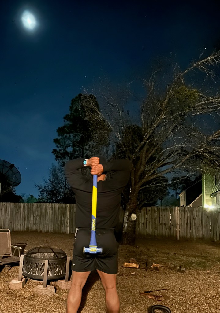 Man swinging a sledgehammer for exercise under the morning moonlight
