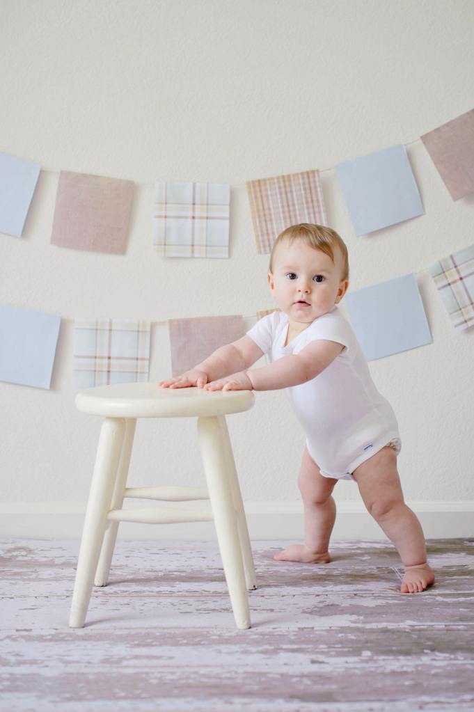Toddler standing by holding on to a stool