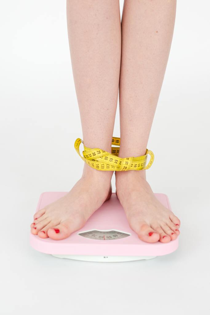 Women standing on scale bound at the ankles with measuring tape